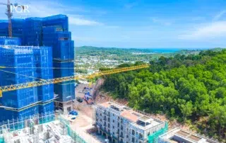 Ảnh giai đoạn xây dựng Hillside với công trình bọc lưới xanh bên trái, sườn đồi bên phải và biển ở xa